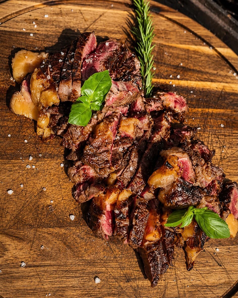 Gesneden gegrilde steak met basilicum en rozemarijn op een houten plank