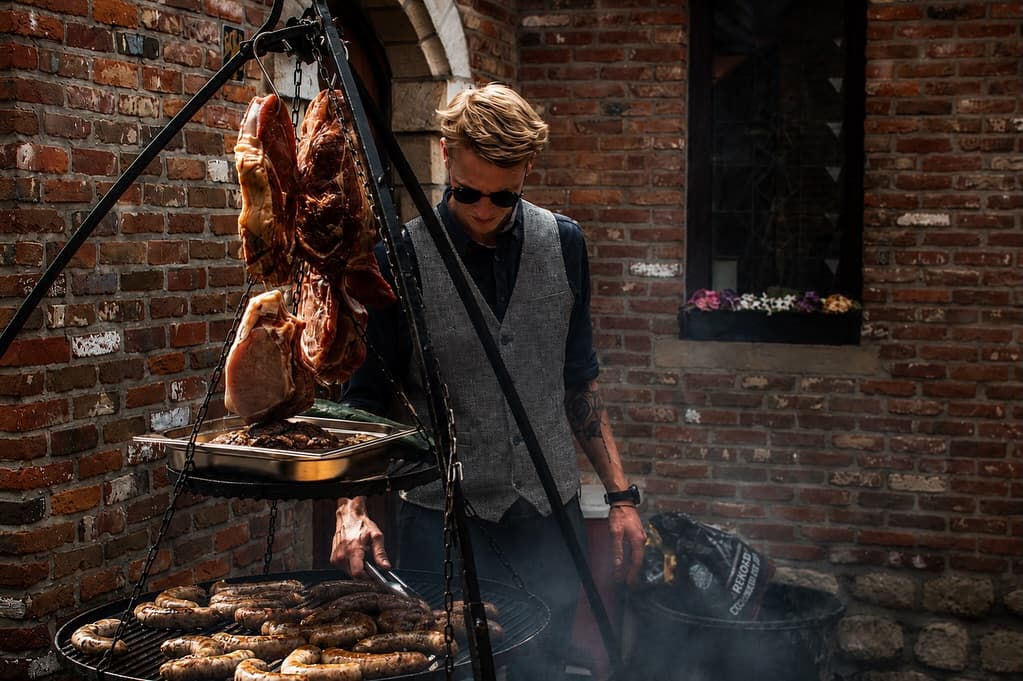 Chef bij een tripod-grill met hangend vlees boven het vuur
